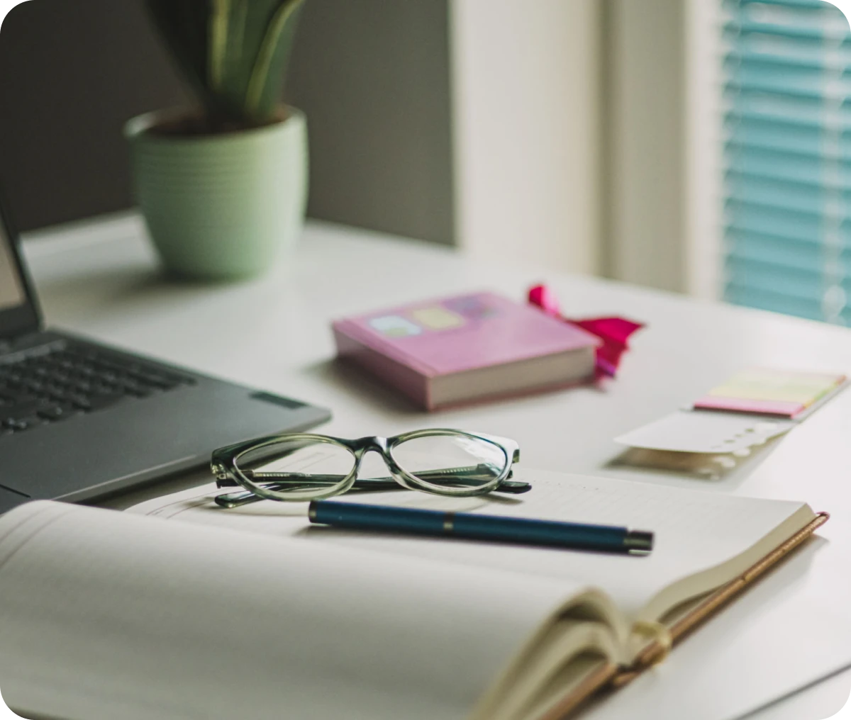 Open book, glasses, laptop on desk.